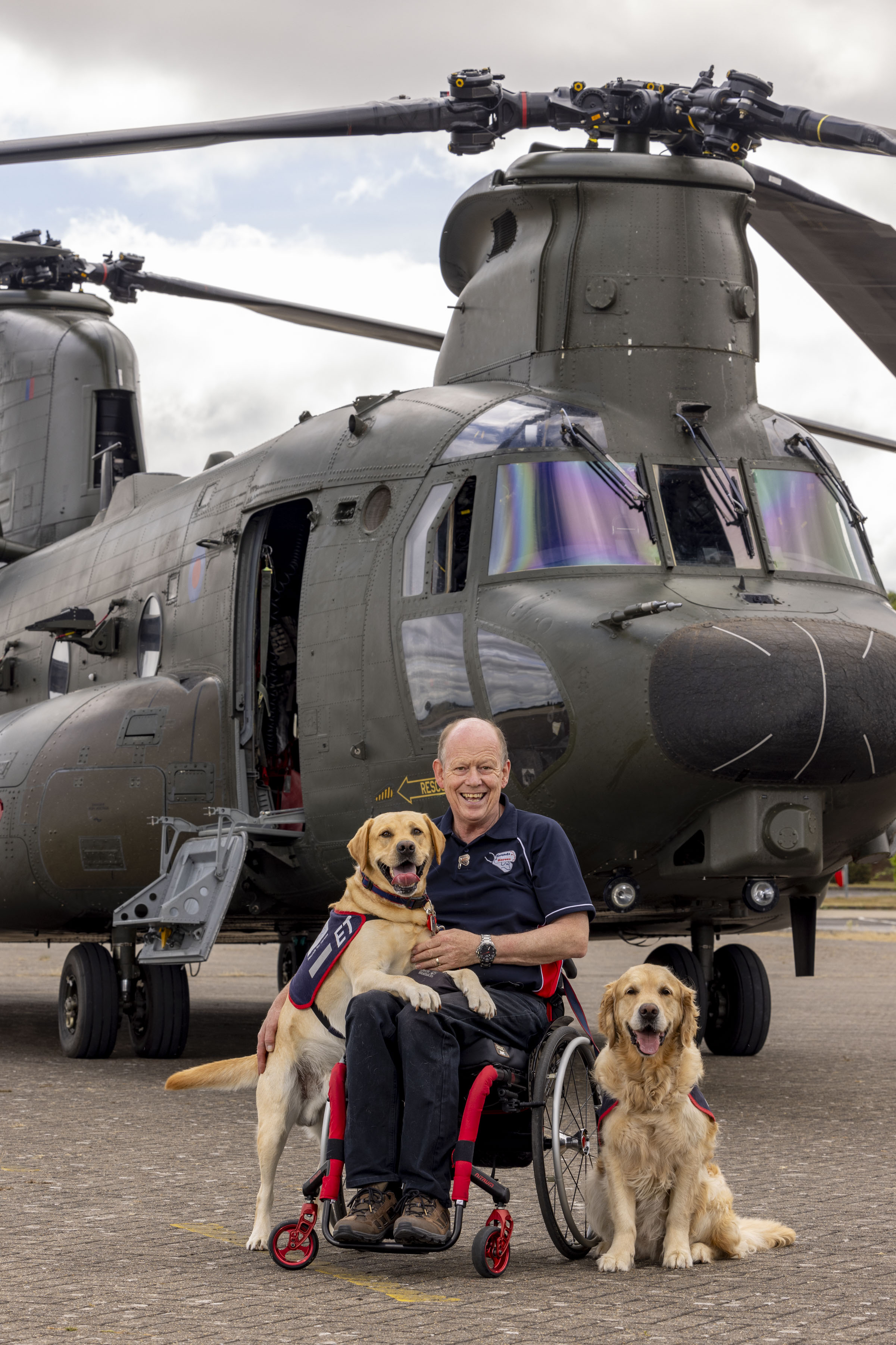 Allen Parton founder of Hounds for Heroes with assistant dogs ET and Flanders. Backdrop is a Chinook helicopter. 