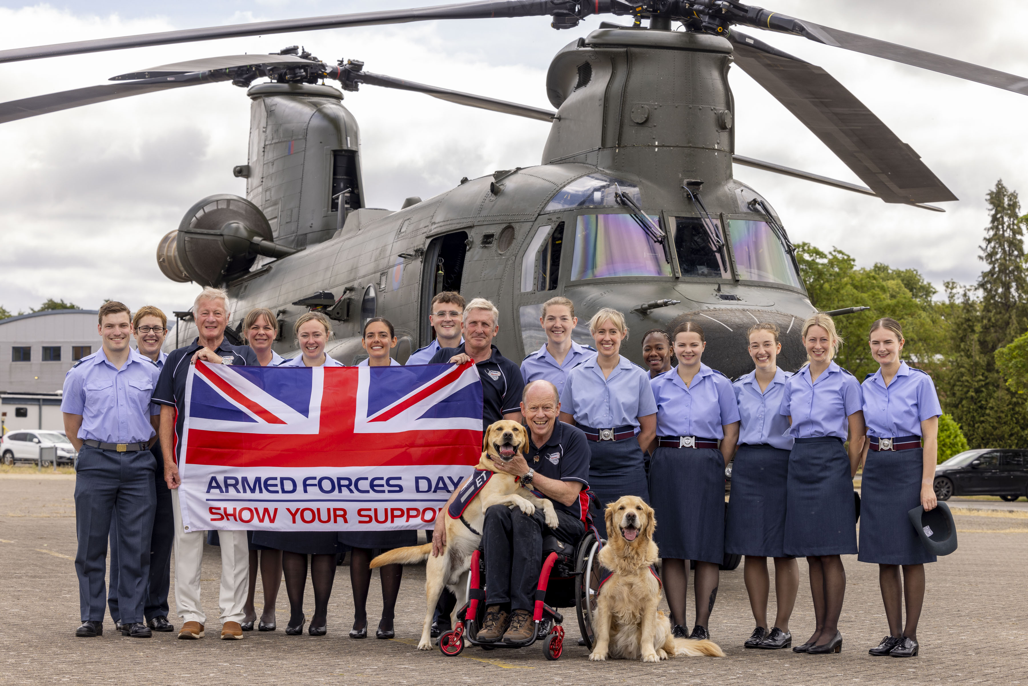 RAF medical staff and Hounds for Heroes staff stood behind Royal Navy Veteran and founder of Hounds for Heroes, Allen Parton. Backdrop a Chinook helicopter and Armed Forces Day Flag. 