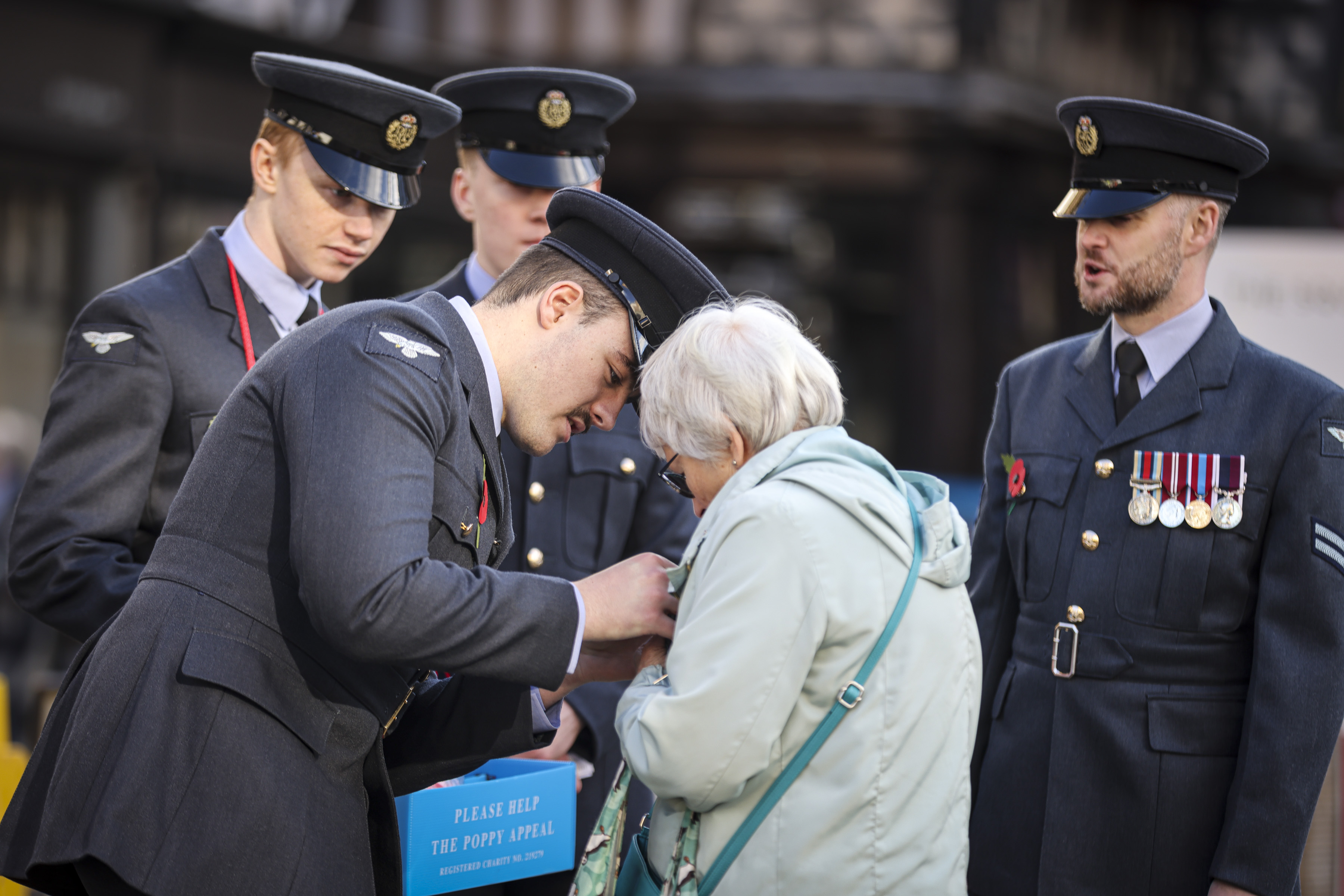 An RAF Cosford Apprentice helps place a poppy on a supporter on their coat within Shrewsbury town centre. 