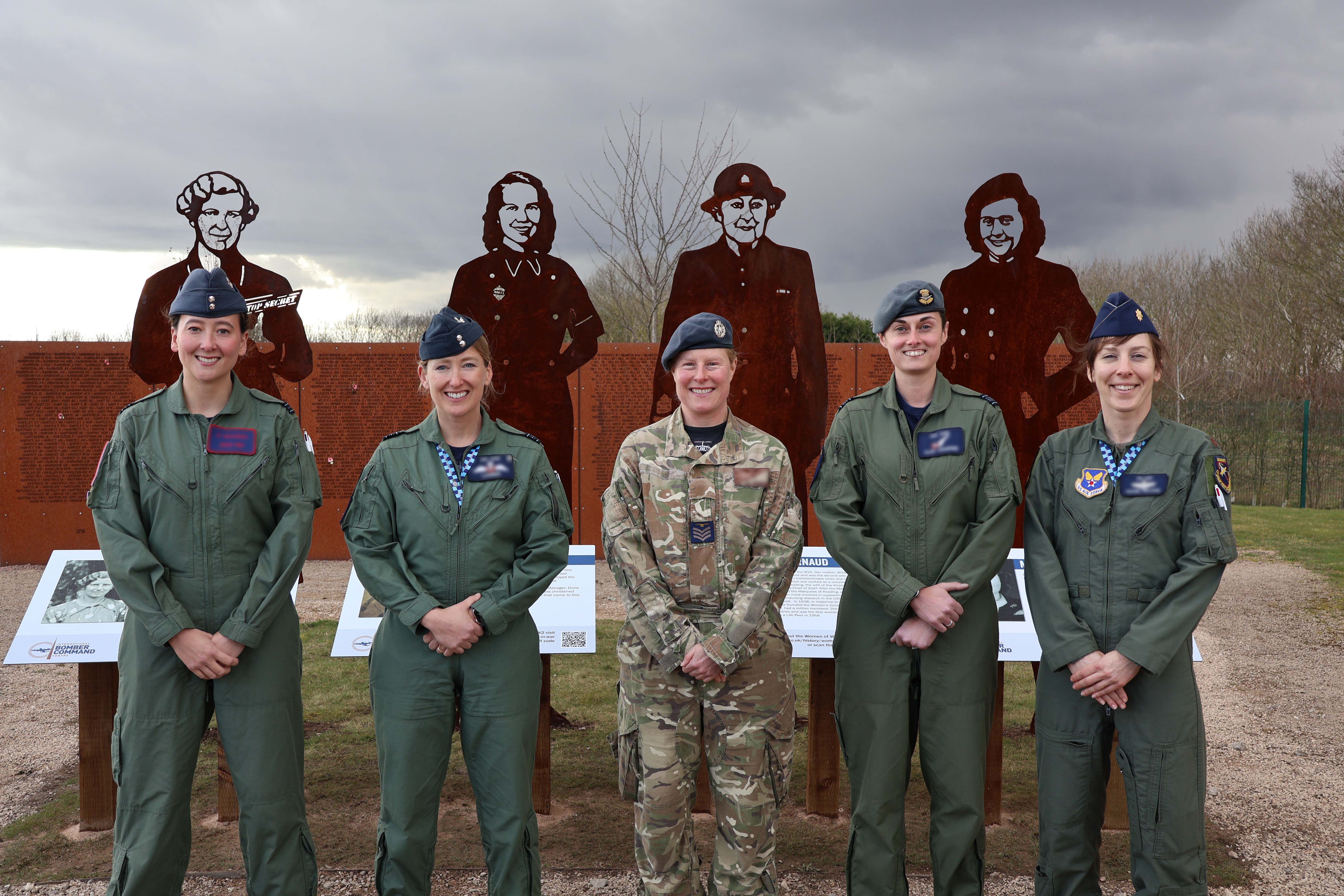 Five female RAF personnel standing in front of the steel silhouette memorial.
