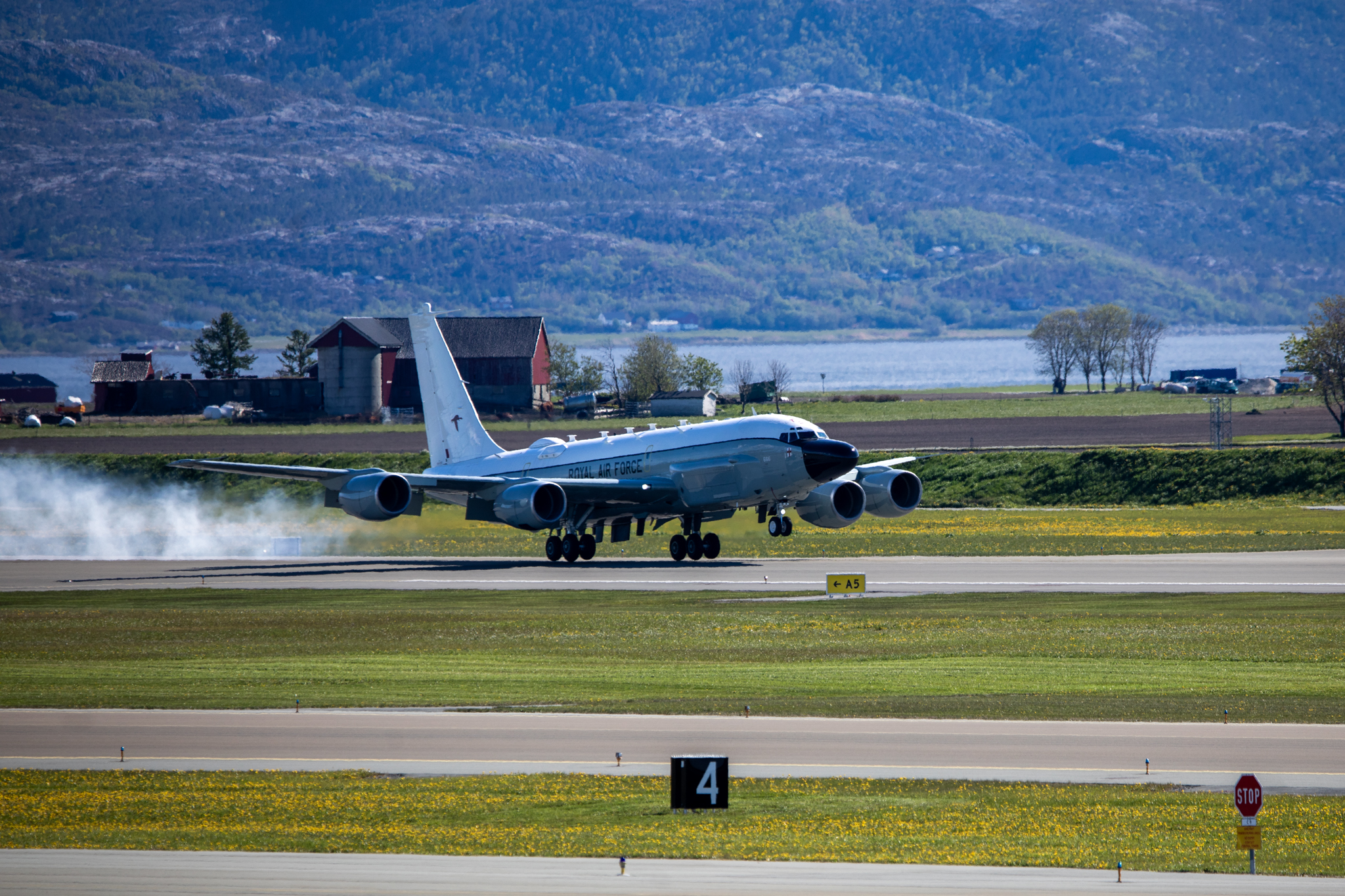RAF Rivet Joint landing on a runway with grassy fields and a coastline in the background.