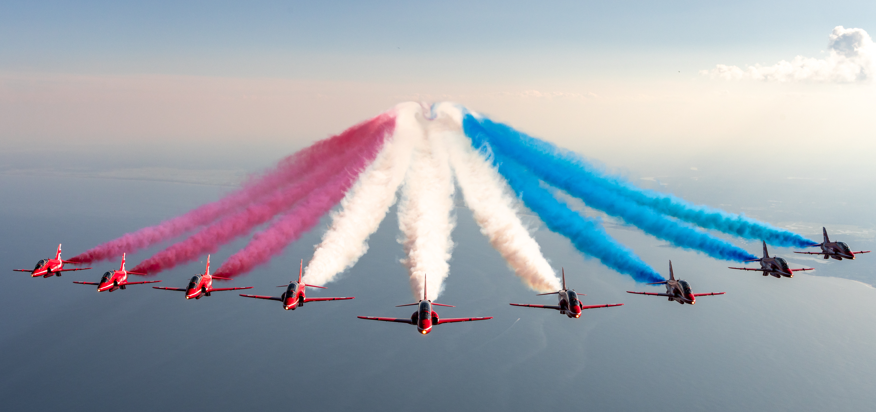 Nine jets from the Red Arrows fly towards the camera trailing red, white and blue smoke colours.