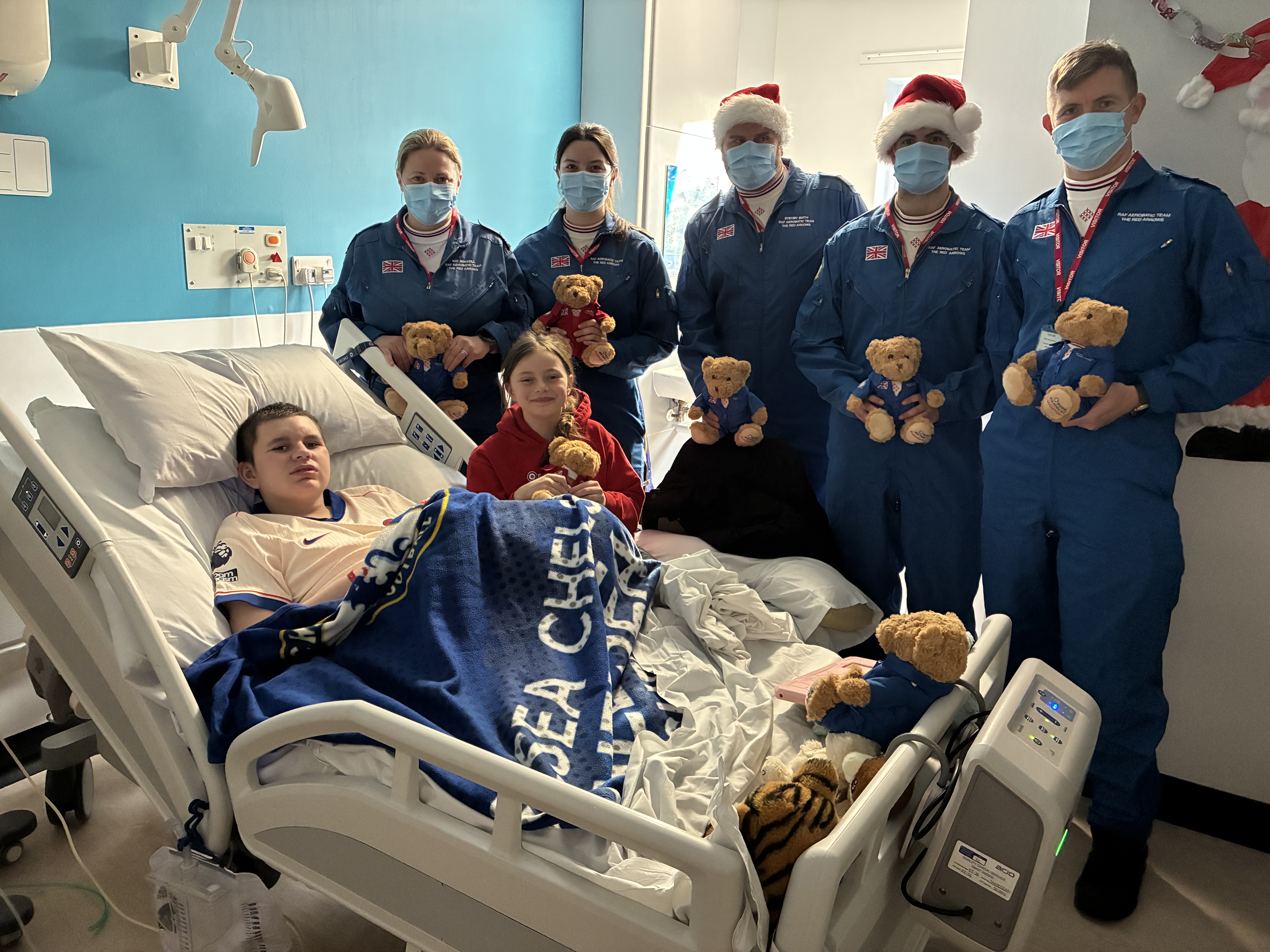 Teddies and other gifts being handed to a patient in a bed by Red Arrows personnel.