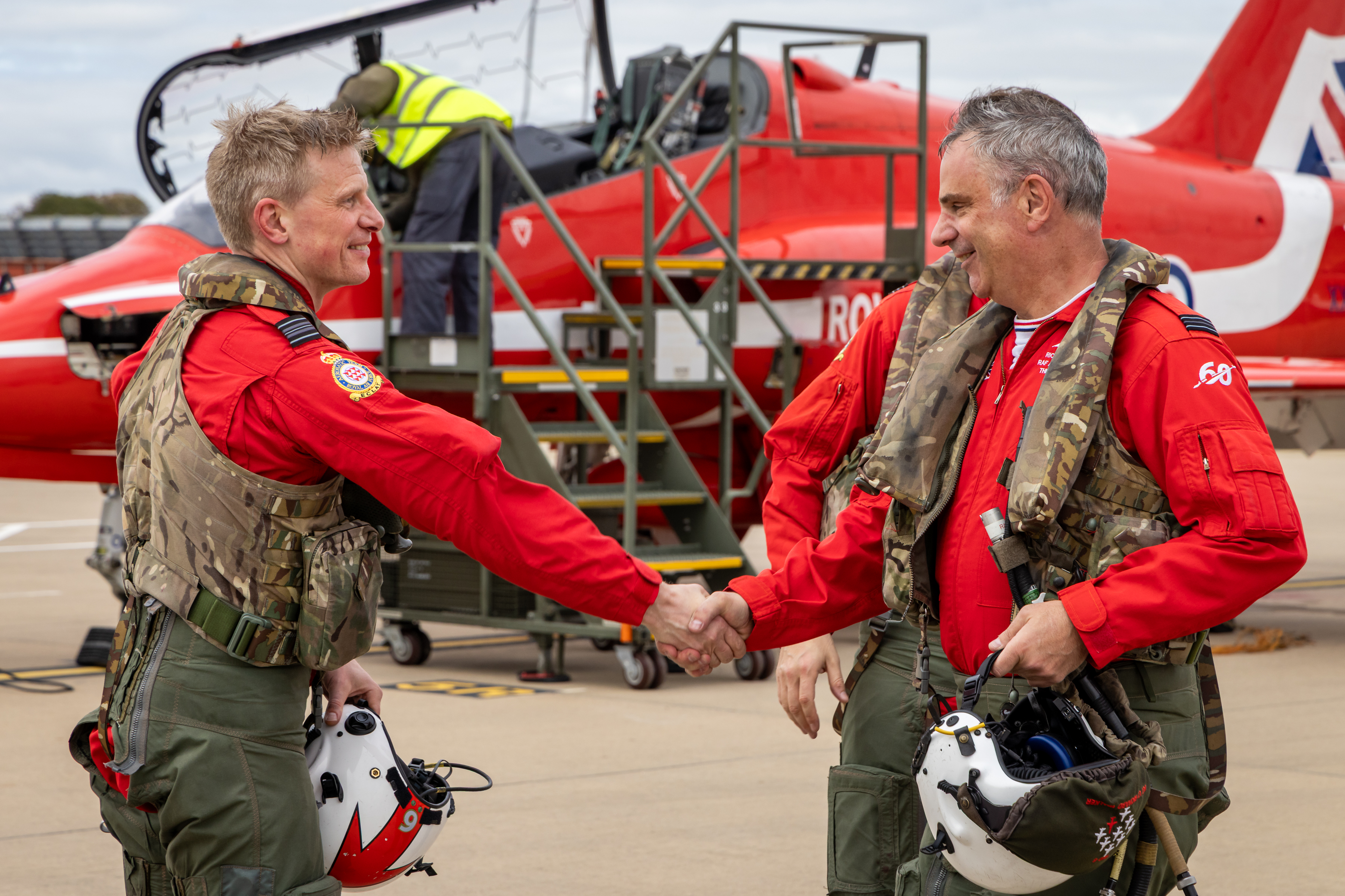 Red 6, left, and Red 8, right, shake hands in front of Hawk jets at RAF Waddington after completing their final flights with the Red Arrows.