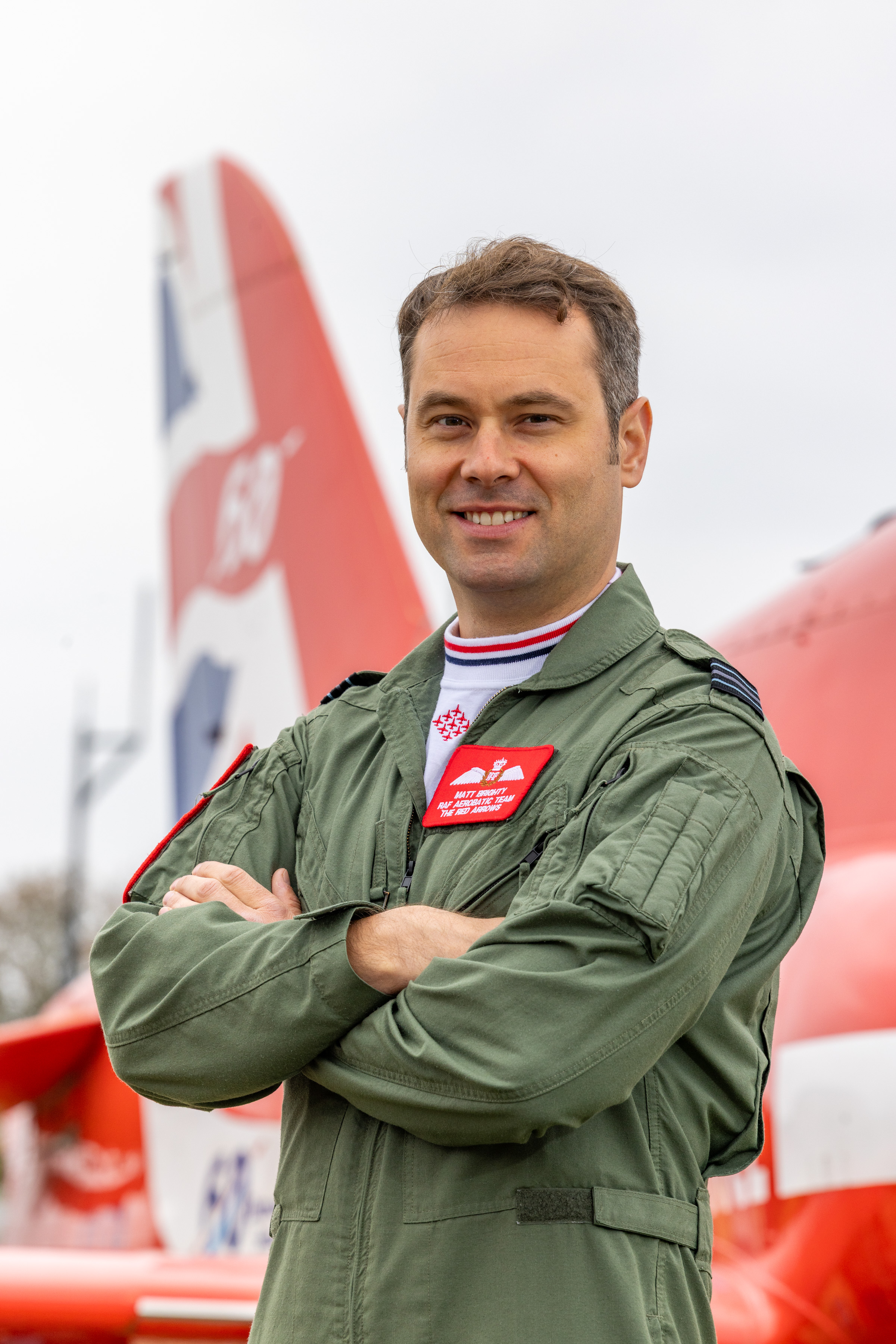 Joining for 2026 - this is Red Arrows pilot Flight Lieutenant Matt Brighty, wearing a green flying coverall, in front of a Red Arrows Hawk jet.