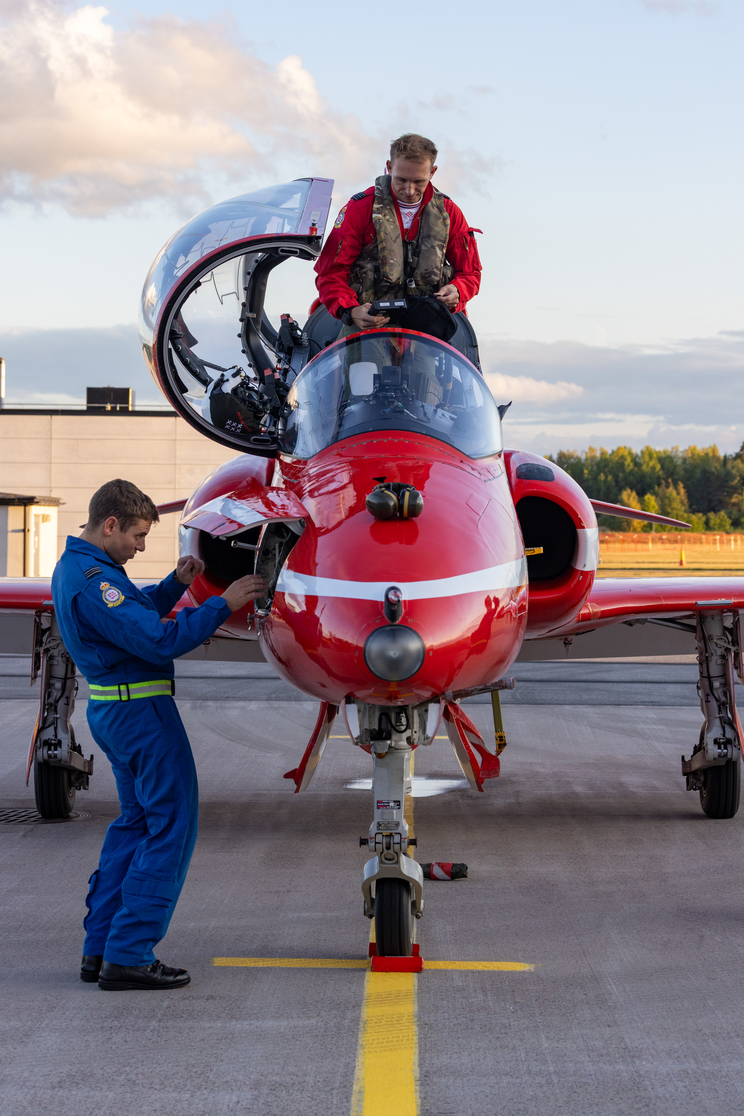 An engineer works on a Red Arrows jet while a pilot steps out of the aircraft.
