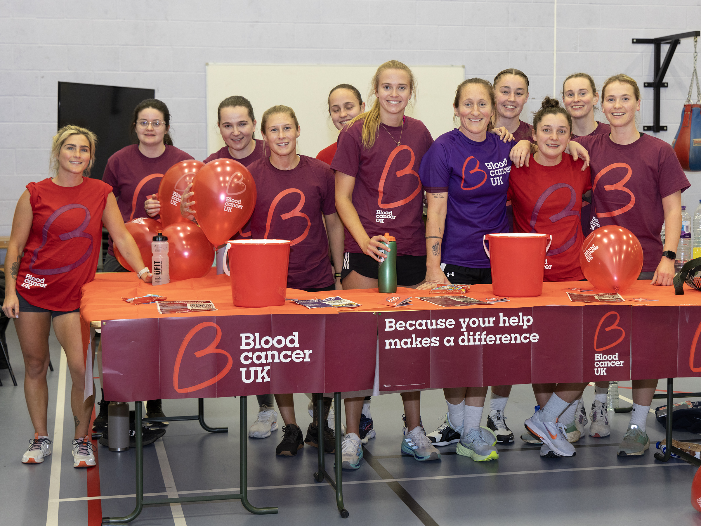 Group of people stand behind a table with balloons and buckets for money collecting.
