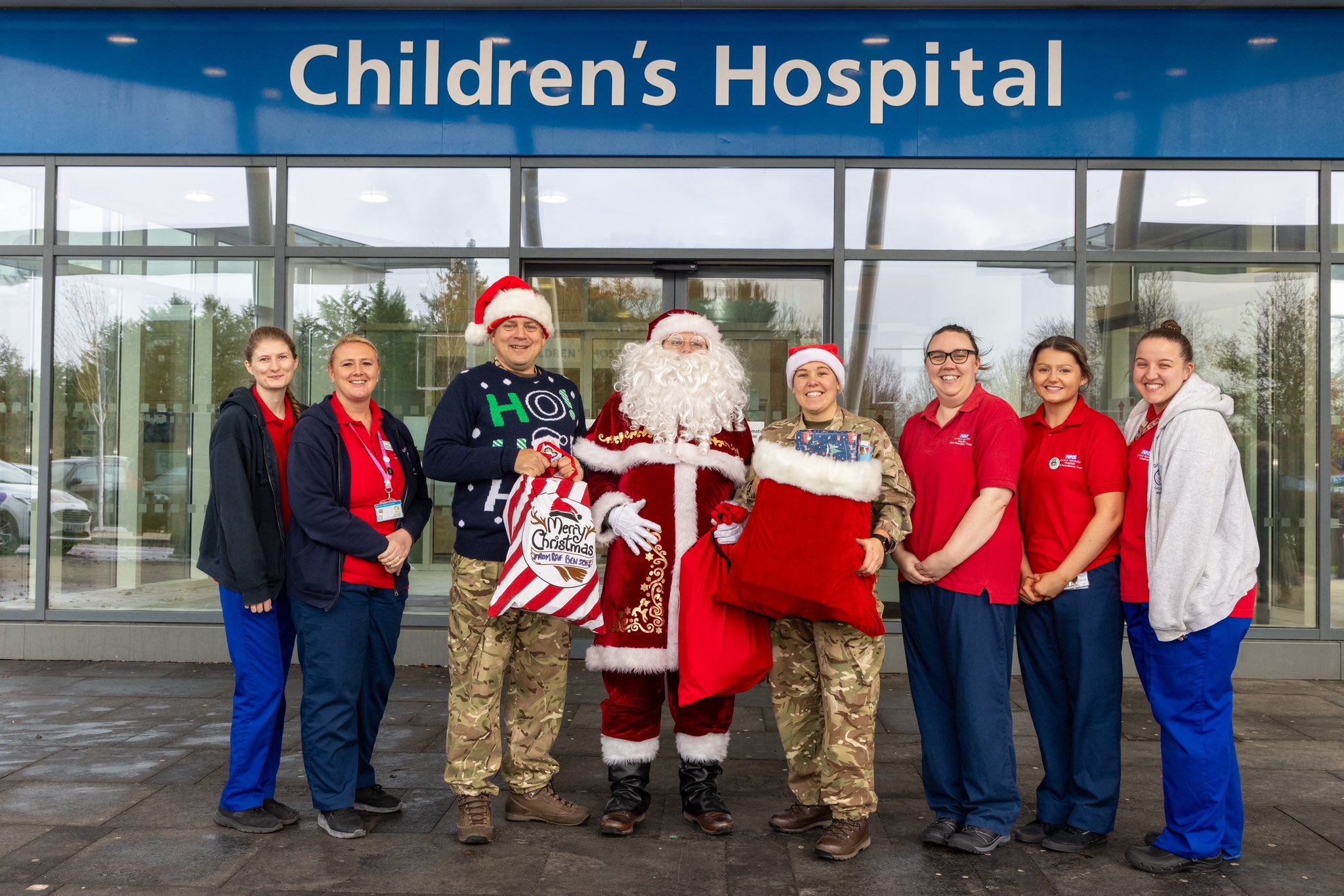 Santa standing with two servicepeople and NHS personnel holding gifts outside of the hospital.