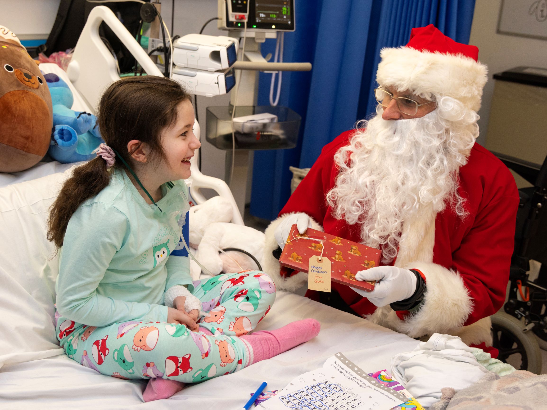 Santa gives a gift to a child on a hospital bed.