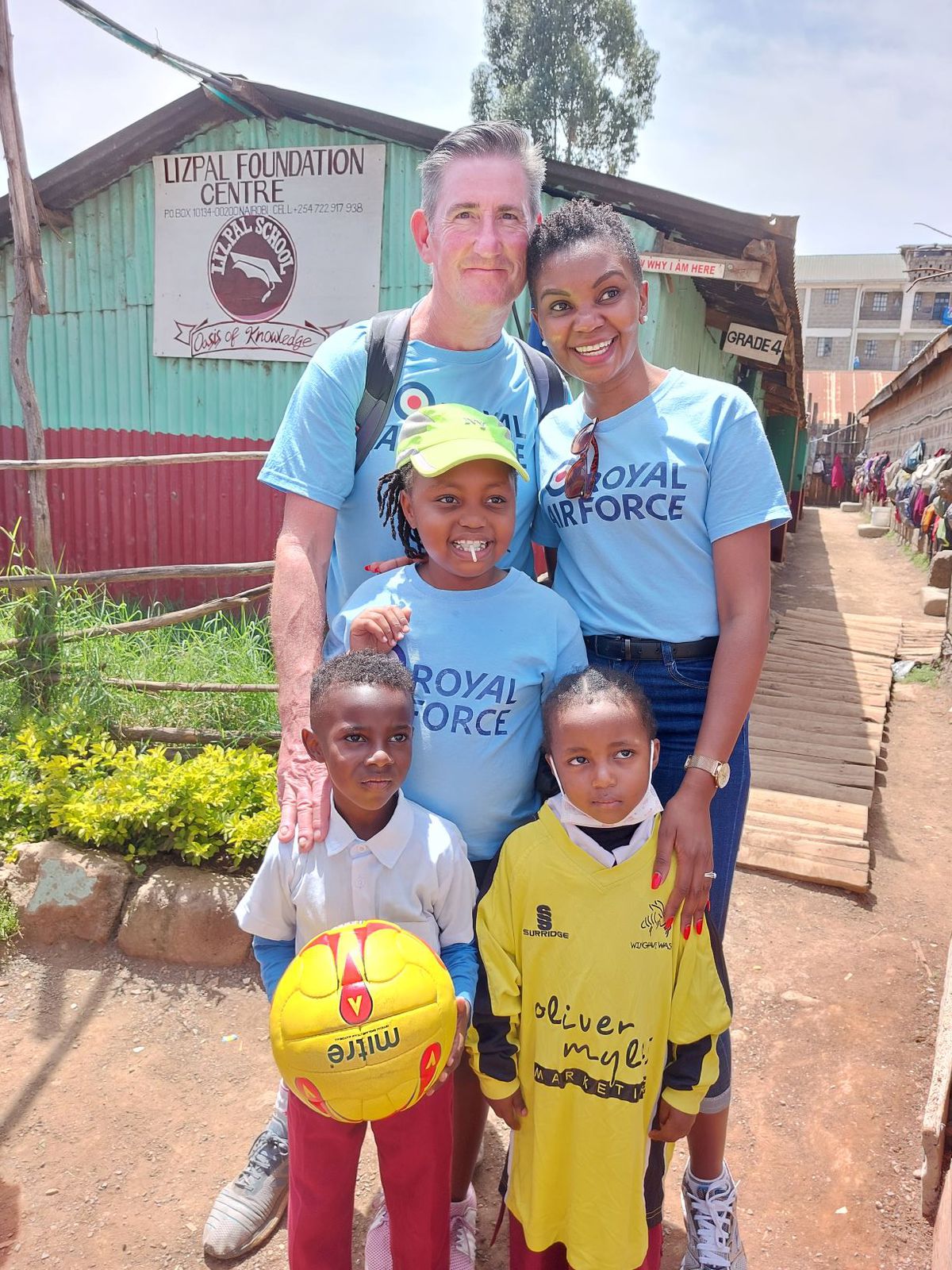 Five people standing outside of the Lipzal Foundation centre, one holding a football.