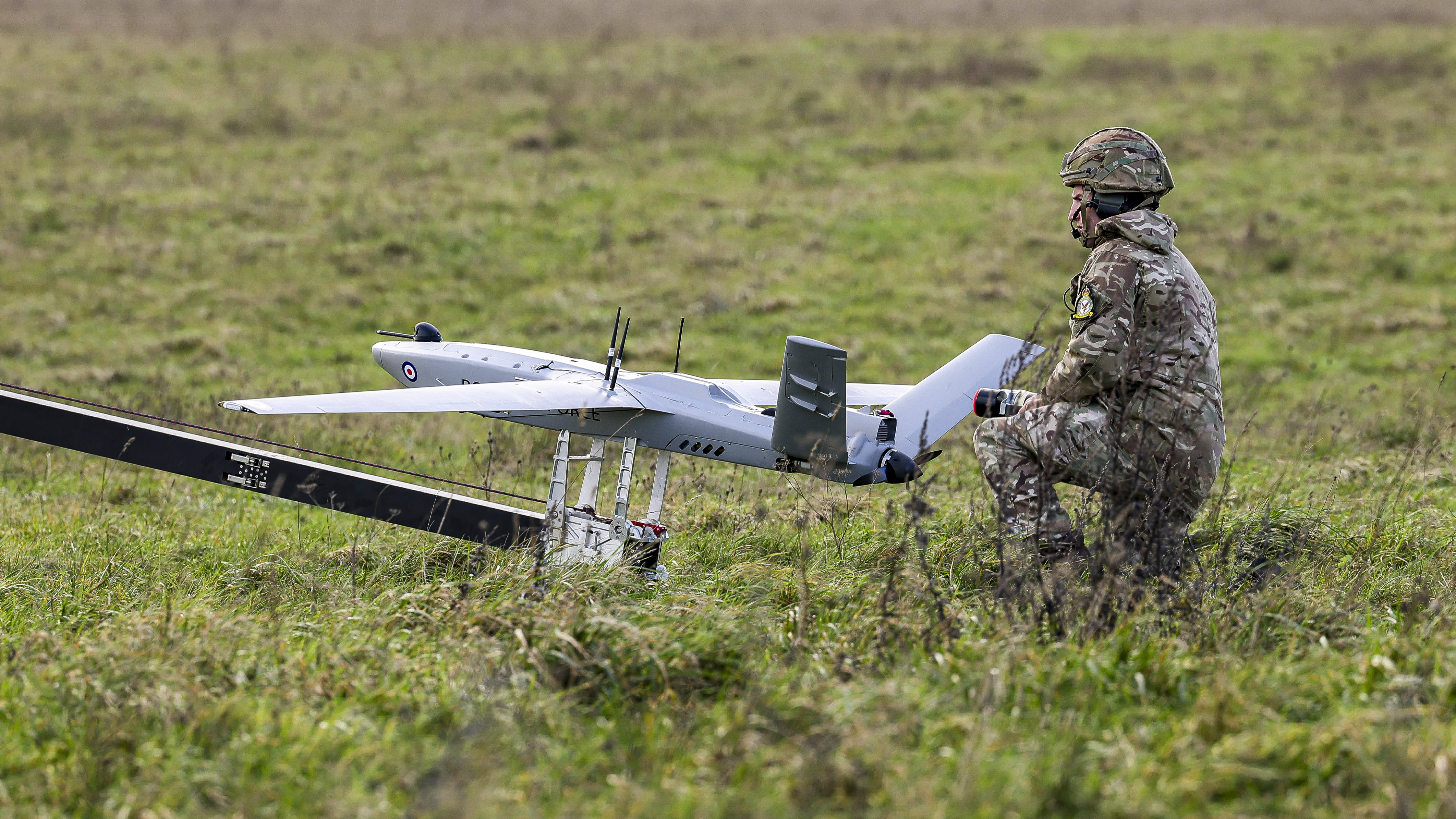 An operator kneels beside a StormShroud drone mounted on a launch rail in an open field, with grass and trees in the distance.